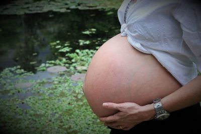 Midsection of pregnant woman standing by pond