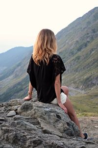 Rear view of woman sitting on rock against clear sky