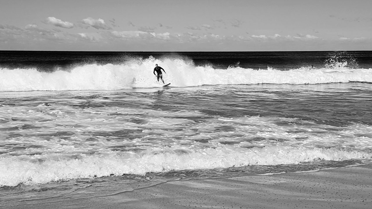 sea, wave, water, motion, one person, real people, nature, beauty in nature, leisure activity, outdoors, extreme sports, sky, men, beach, standing, scenics, lifestyles, day, sport, horizon over water, full length, power in nature, people