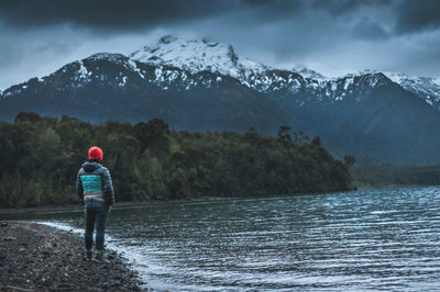 Rear view of person standing on snowcapped mountain against sky