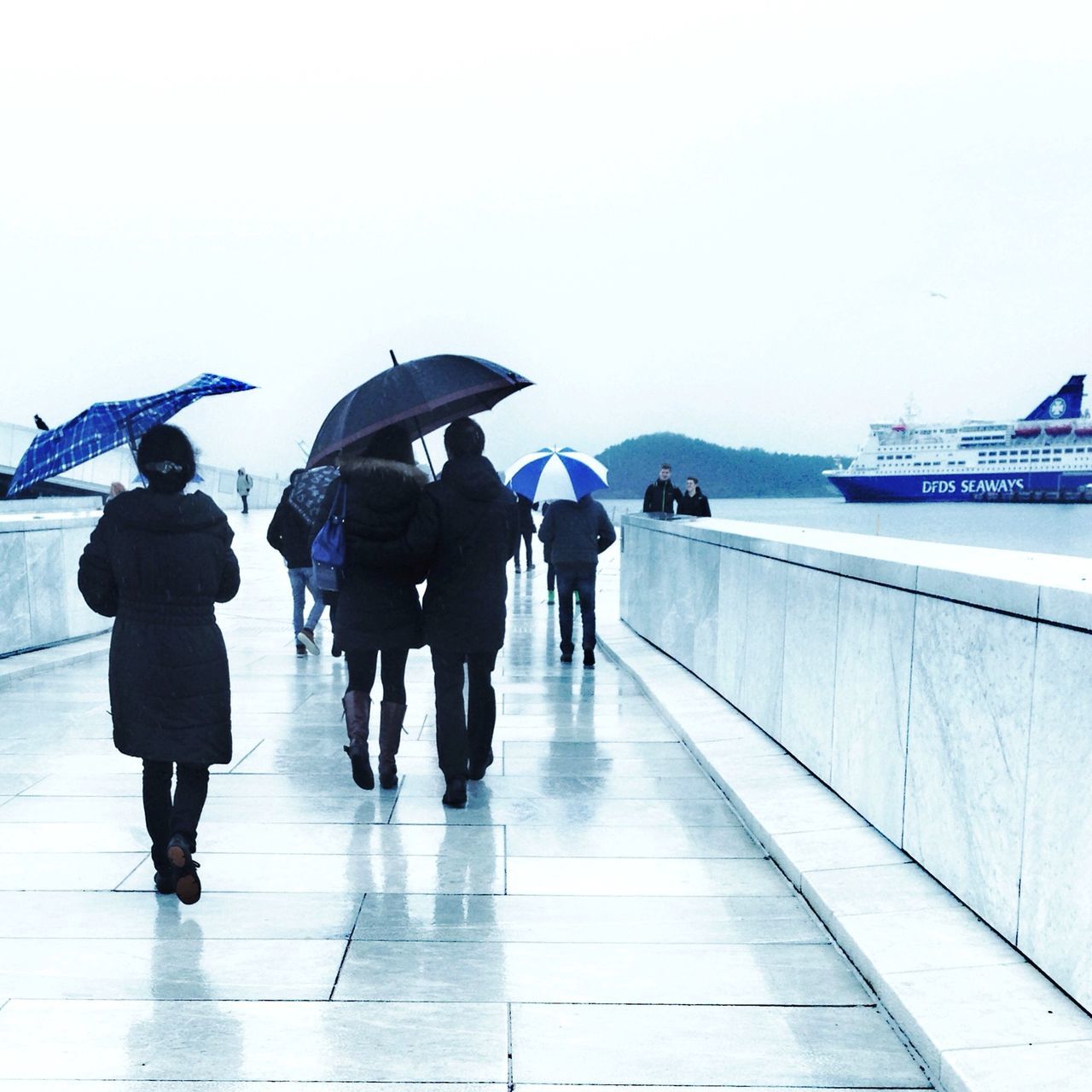 full length, walking, water, rear view, clear sky, men, lifestyles, leisure activity, person, copy space, sea, standing, casual clothing, umbrella, built structure, railing, day, sky, reflection