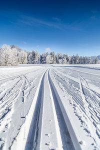 Tire tracks on snow covered land against blue sky