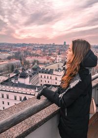 Side view of woman looking at cityscape against sky during sunset