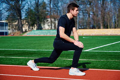 Man in sport clothers does a warm-up exercises at stadium track before jogging outdoors