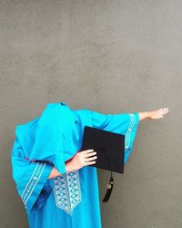 Woman holding mortar board while gesturing while standing against wall