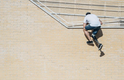 Young man with leg prosthesisclimbing up brick wall