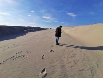 Rear view of man walking in desert against sky