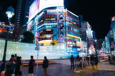 People walking on illuminated street amidst buildings in city at night