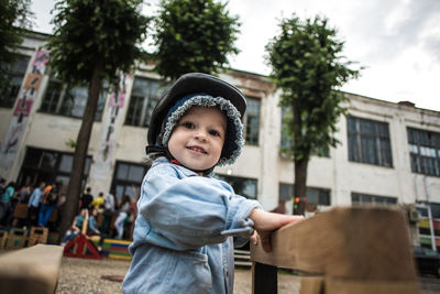 Portrait of boy wearing cap by wooden play equipment against building