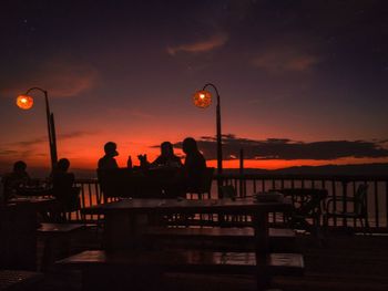 Silhouette people sitting by sea at restaurant during sunset
