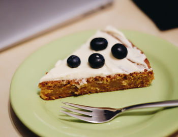 Slice of carrot cake with blueberry on top served in plate with fork
