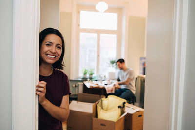 Portrait of smiling woman leaning on doorway at new home
