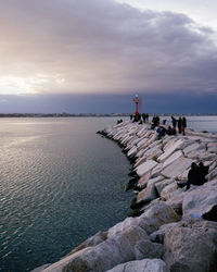 Group of people on rock by sea against sky