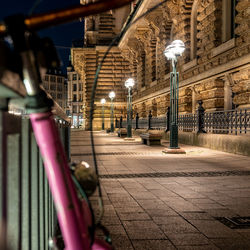 Illuminated street light on footpath against buildings in city