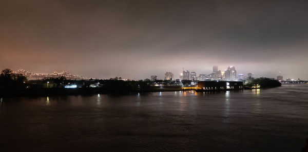 Illuminated city by river against sky at night