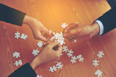 High angle view of people holding jigsaw piece on table