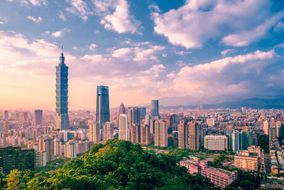 Aerial view of modern buildings against cloudy sky in city during sunset