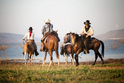 Men riding horse on grass against lake and sky