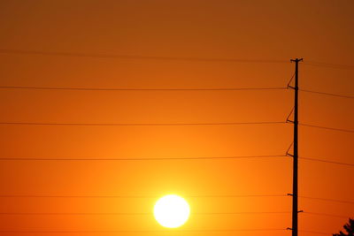 Low angle view of silhouette electricity pylon against orange sky