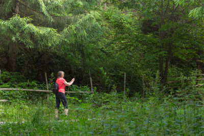 Side view of woman photographing with mobile in forest