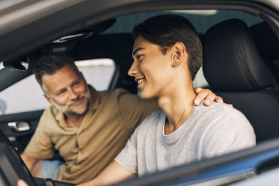 Smiling young man getting driving lessons from father while sitting in car