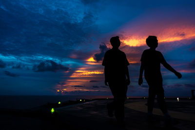 Silhouette friends standing on beach against sky at sunset