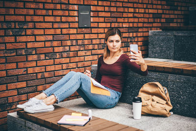 Low angle view of young woman sitting against brick wall