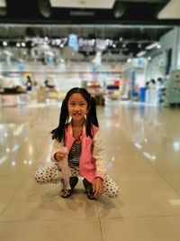 Smiling girl crouching on tiled floor in shopping mall