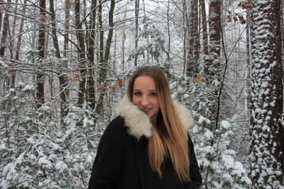 Portrait of beautiful young woman in warm clothing standing at forest during winter