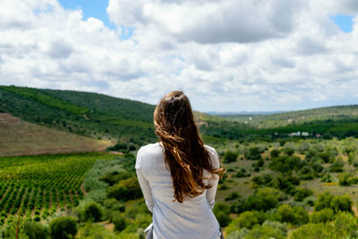 Rear view of woman sitting on mountain against cloudy sky