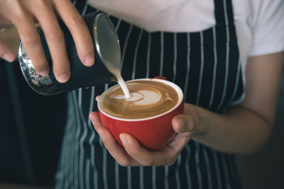 Midsection of woman pouring milk in coffee cup