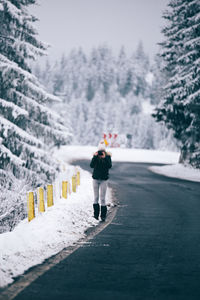 Full length of woman photographing with camera while standing on road during winter