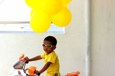 Boy sitting on toy motorcycle by balloons