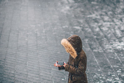 Woman using mobile phone while standing on road during winter