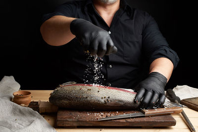 Midsection of man holding white salt and fish salmon on table