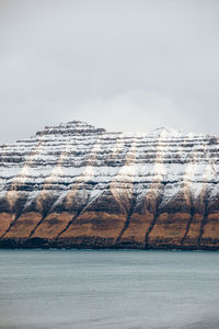 Majestic scenery of rocky terrain covered with snow near calm sea on cloudy day on faroe islands