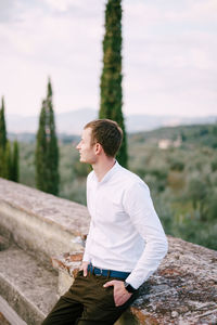 Young man looking away while sitting on land against sky