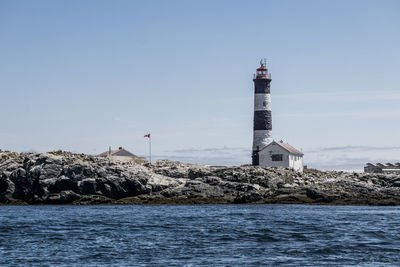 Lighthouse by sea against buildings against clear sky