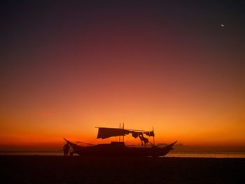 Silhouette man standing by outrigger moored at beach during sunset