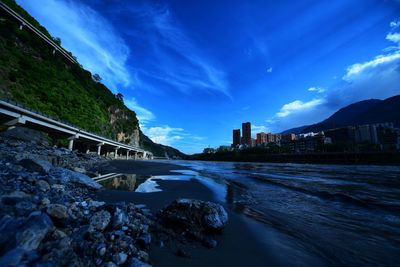 Bridge over river by city against blue sky