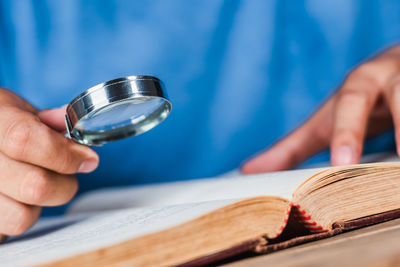 Midsection of man holding magnifying glass over book on table