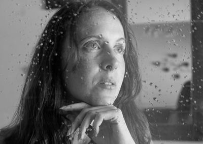 Portrait of woman looking through wet window in rainy season