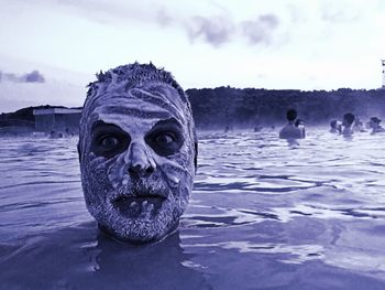 Close-up of man with white mud on face swimming in lagoon