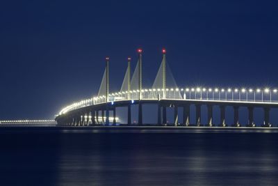 Illuminated penang bridge over strait of malacca against clear sky at night