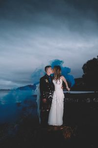 Full length of couple kissing on the mouth while standing amidst smoke against sky