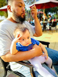 Father holding baby boy while sitting on chair