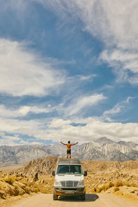Young man on roof of van with outstretched arms in northern california