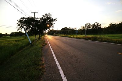 Road amidst field against clear sky at sunset