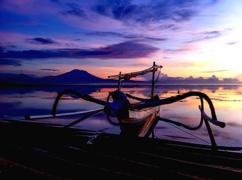 Outrigger canoe moored at lakeshore against sky during sunset