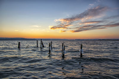 Silhouette wooden posts in sea against sky during sunset